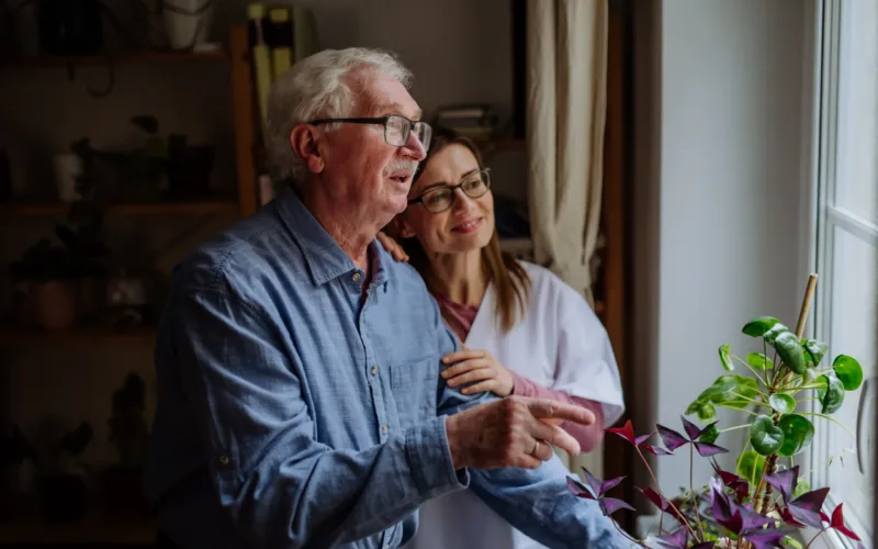 A healthcare worker or caregiver visiting senior man indoors at home, talking.