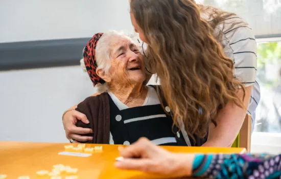 Senior woman laughing with caregiver in the nursing home while playing board skill game